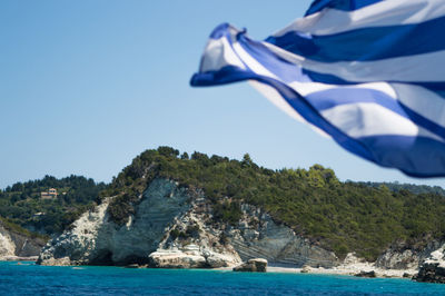 Greek flag waving against rocky mountain by sea