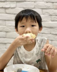 Portrait of boy eating food against wall