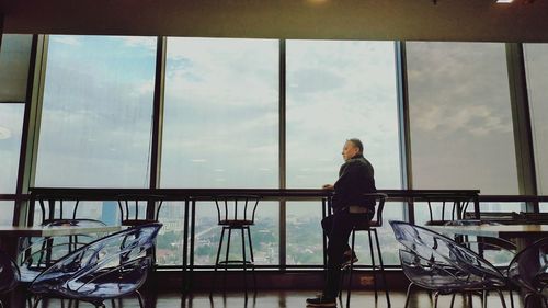 Man sitting on chair against sky seen through glass window