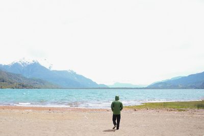 Rear view of man standing on beach against clear sky