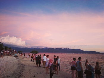 People at beach against sky during sunset