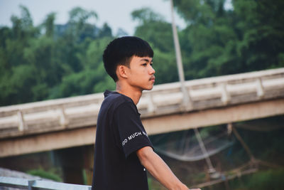 Boy looking away while standing against trees