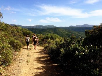 Rear view of men walking on mountain road against sky