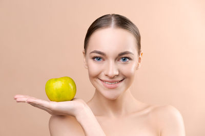 Portrait of young woman holding apple against pink background