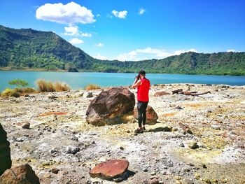 Man standing on rock looking at shore against sky