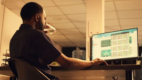 Rear view of man using laptop at home