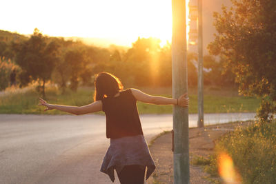 Rear view of playful young woman holding pole by road