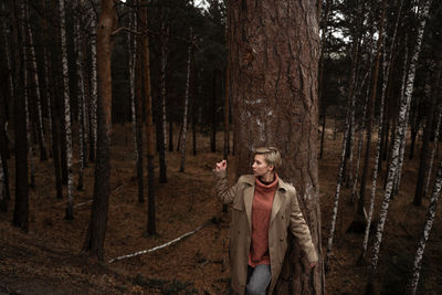 Young woman standing by tree trunk in forest