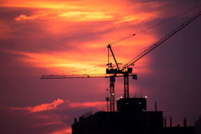 Low angle view of silhouette cranes against cloudy sky during sunset