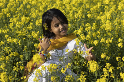 Smiling girl sitting amidst yellow flowers