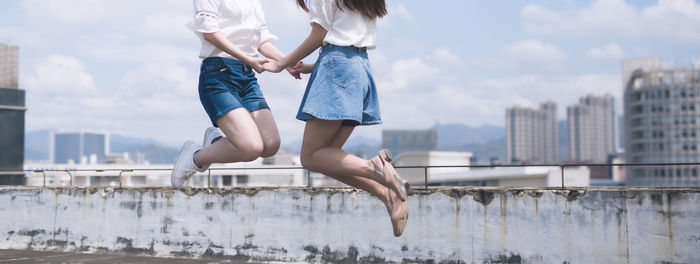 Low section of women jumping in city against sky