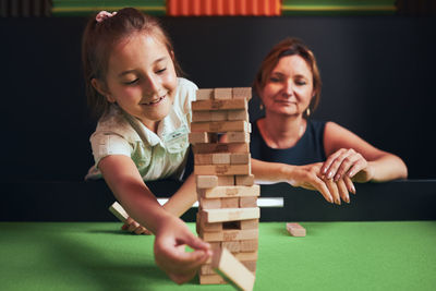 Mother and her daughter playing jenga game together in play room. girl removing one block from stack