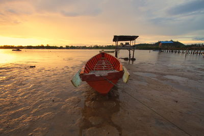 Boat moored on beach against sky during sunset