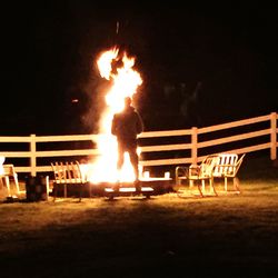 Man standing against illuminated fire at night