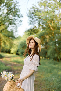 Side view of young woman standing against trees