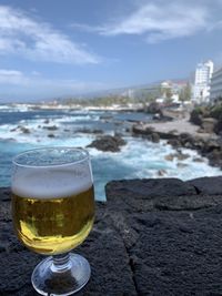 Close-up of beer glass on beach against sky