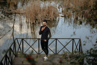 Young man using mobile phone while standing on railing