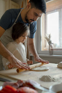 Boy with father rolling pizza dough in kitchen