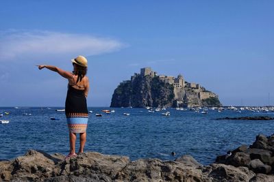 Woman standing on rock by sea against sky