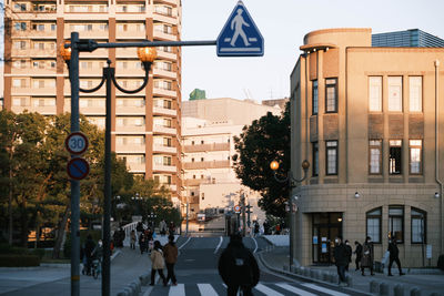 Group of people walking on road against buildings at sunset