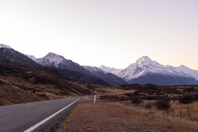 Road leading towards mountains against clear sky