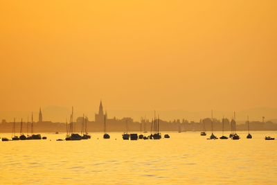 Sailboats in sea against orange sky