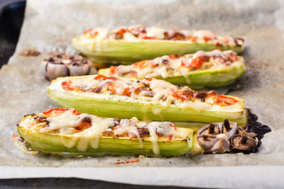 Ready-to-eat baked zucchini halves stuffed with cheese and tomato on baking paper on a baking sheet