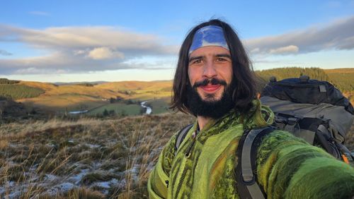 Portrait of young woman standing on field against sky