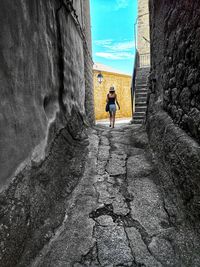 Woman walking in alley amidst buildings against sky