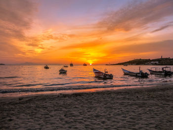 Boats moored on shore at beach against sky during sunset