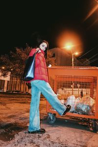 Portrait of young woman sitting on illuminated street at night