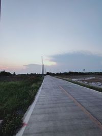 Road amidst field against sky during sunset