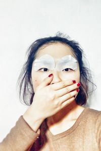 Close-up of woman with hand covering mouth against white background
