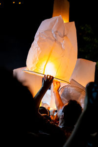 Man releasing illuminated paper lantern at night