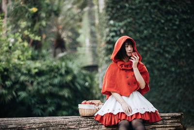 Woman with red umbrella sitting against trees