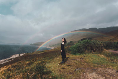 Full length of man standing on field against rainbow in sky