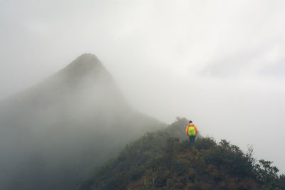 Rear view of man on mountain against sky during foggy weather