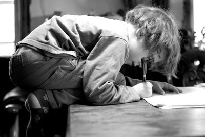 Side view of boy studying while kneeling on table at home