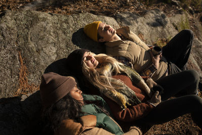 High angle view of male and female friends relaxing on rock during sunny day