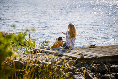 Female talking through smartphone while sitting on jetty over lake