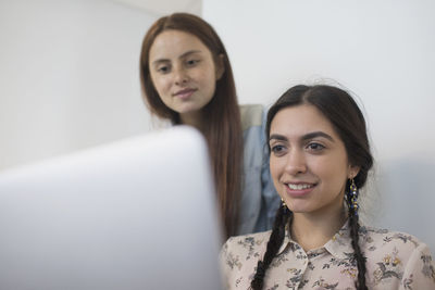 Two young woman working in an office off a laptop.