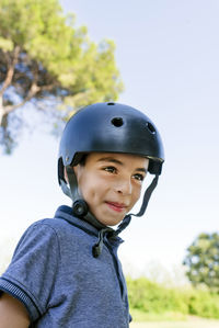 Little boy looking at camera while wearing protective helmet outdoors in a park.