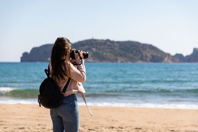 Rear view of woman standing on beach against sky