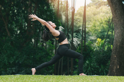 Woman with arms raised exercising against trees