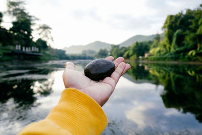 Close-up of person holding pebble over lake against sky
