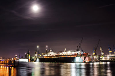 Illuminated commercial dock by sea against sky at night