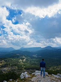 Rear view of man standing on mountain against sky
