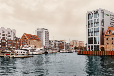 Sailboats moored on river by buildings in city against sky