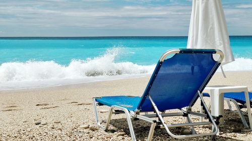 Deck chairs on beach against blue sky