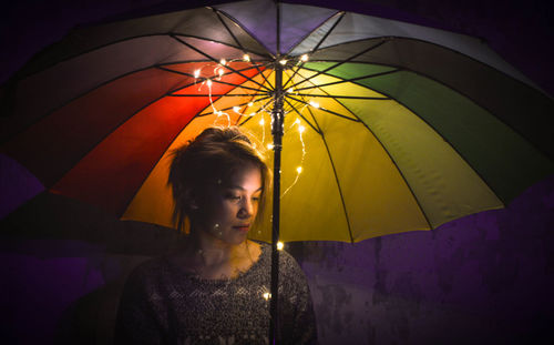 Close-up of young woman holding umbrella with illuminated string lights